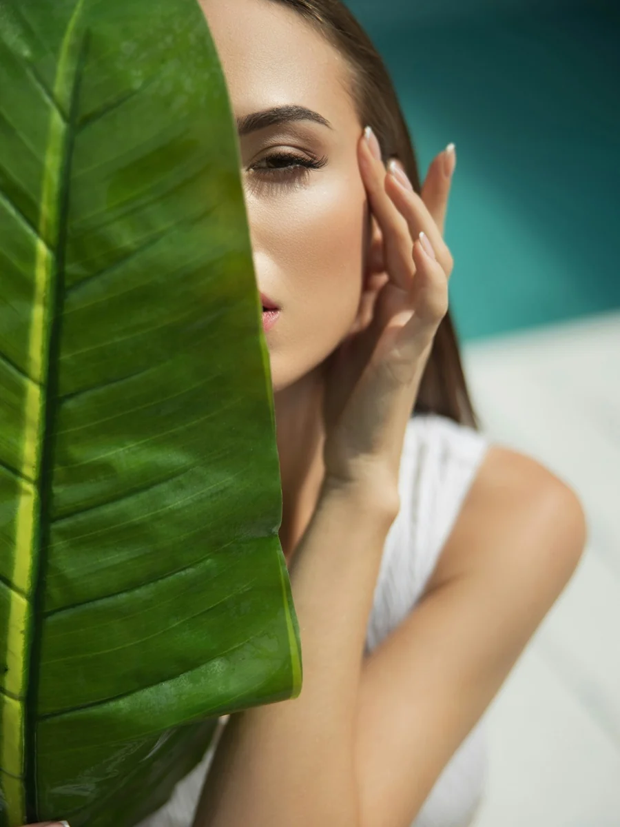 Close-up luxury beauty editorial portrait framed by a tropical green leaf